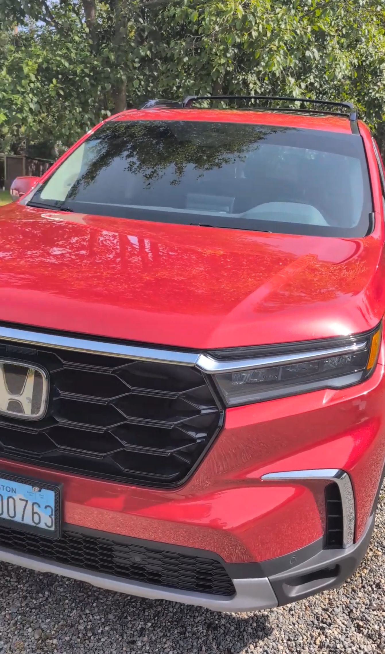 A bright red Honda SUV parked on a gravel surface with trees in the background.