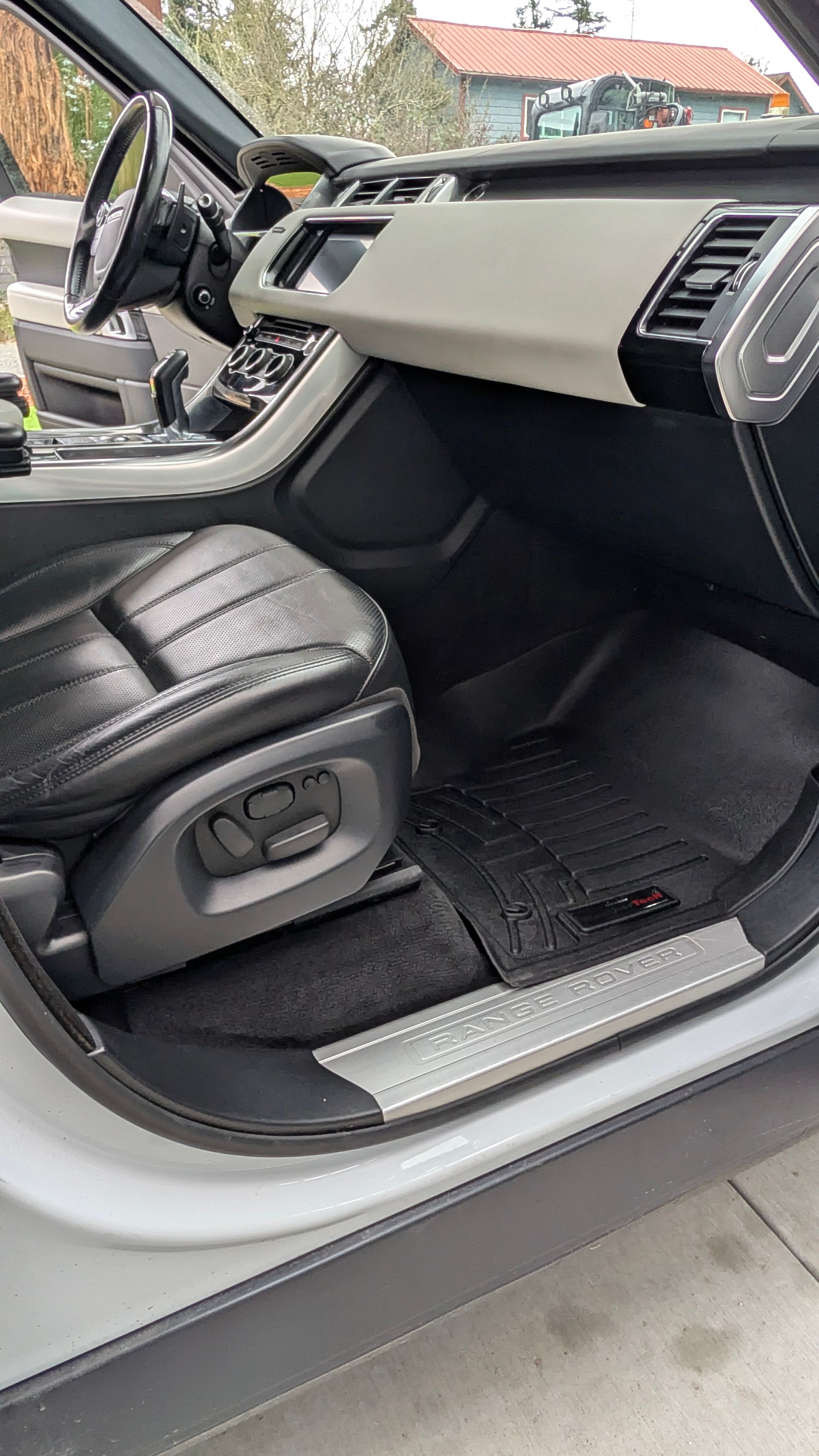 The interior of a vehicle featuring black leather bucket seats, a two-toned dashboard, and textured black floor mats.