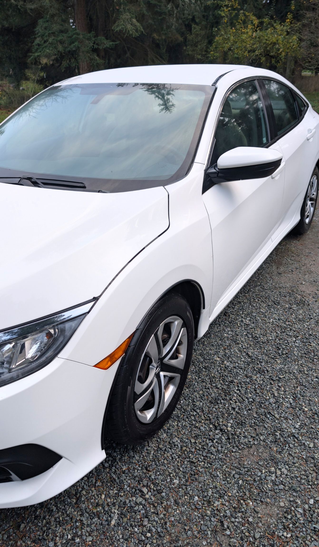 A white sedan parked on a gravel surface, viewed from the front passenger side.