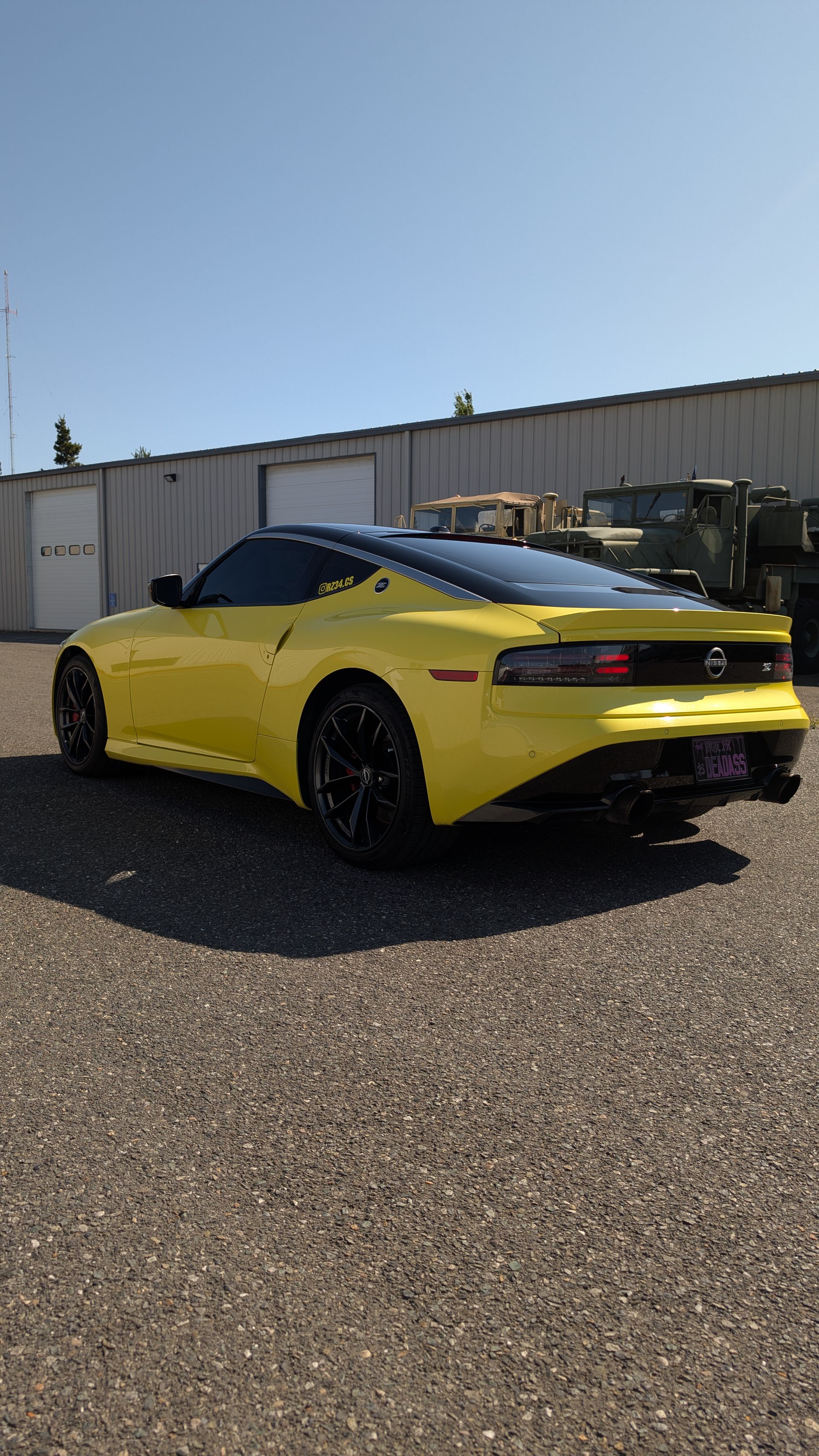 A bright yellow Nissan Z sports car parked on a gravel lot in front of a metal building on a sunny day.