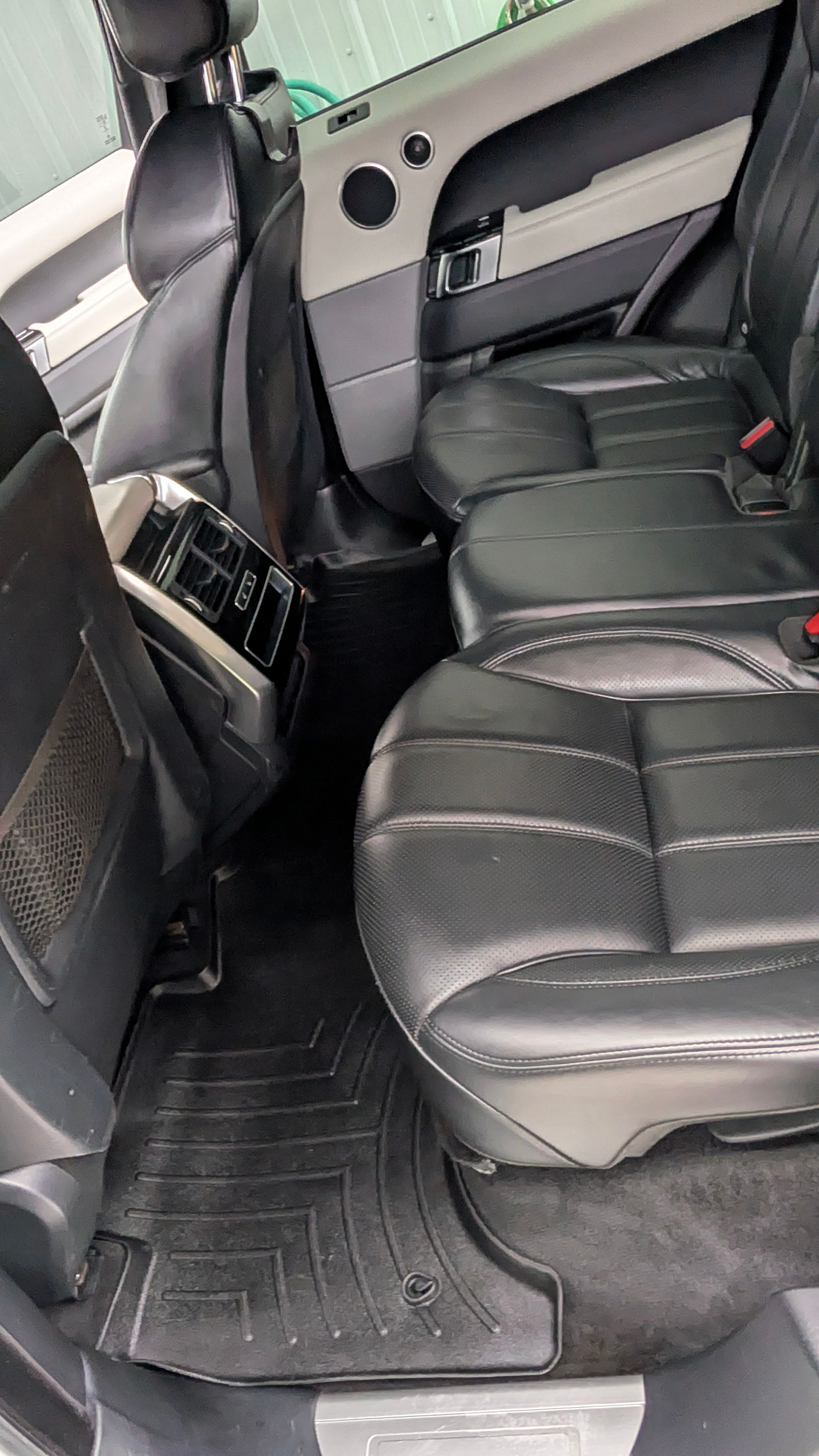 Back seats of a vehicle with black leather upholstery, a central touchscreen, and black all-weather floor mats.