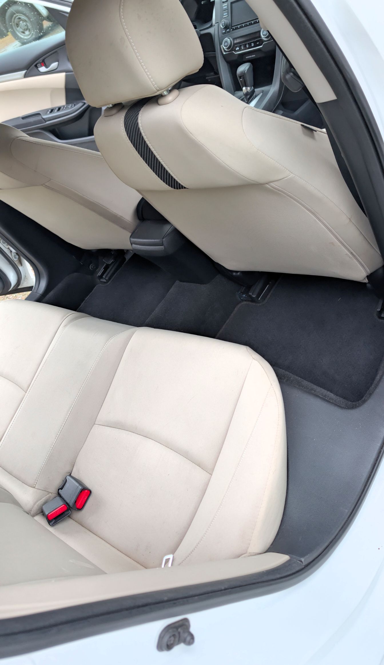 Interior view of a car showing beige leather seats and a black floor mat in the back seating area.