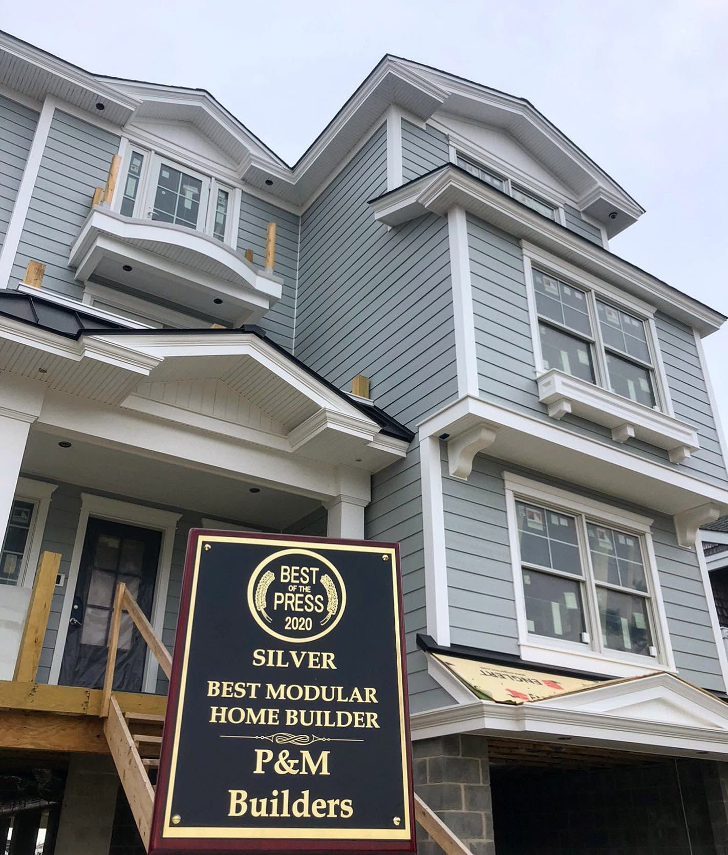 Grey multi-story modular home with a black-and-gold P&M Builders sign in front