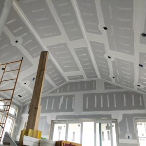 Interior under renovation with unfinished drywall ceiling, scaffolding, and exposed wooden support beam.