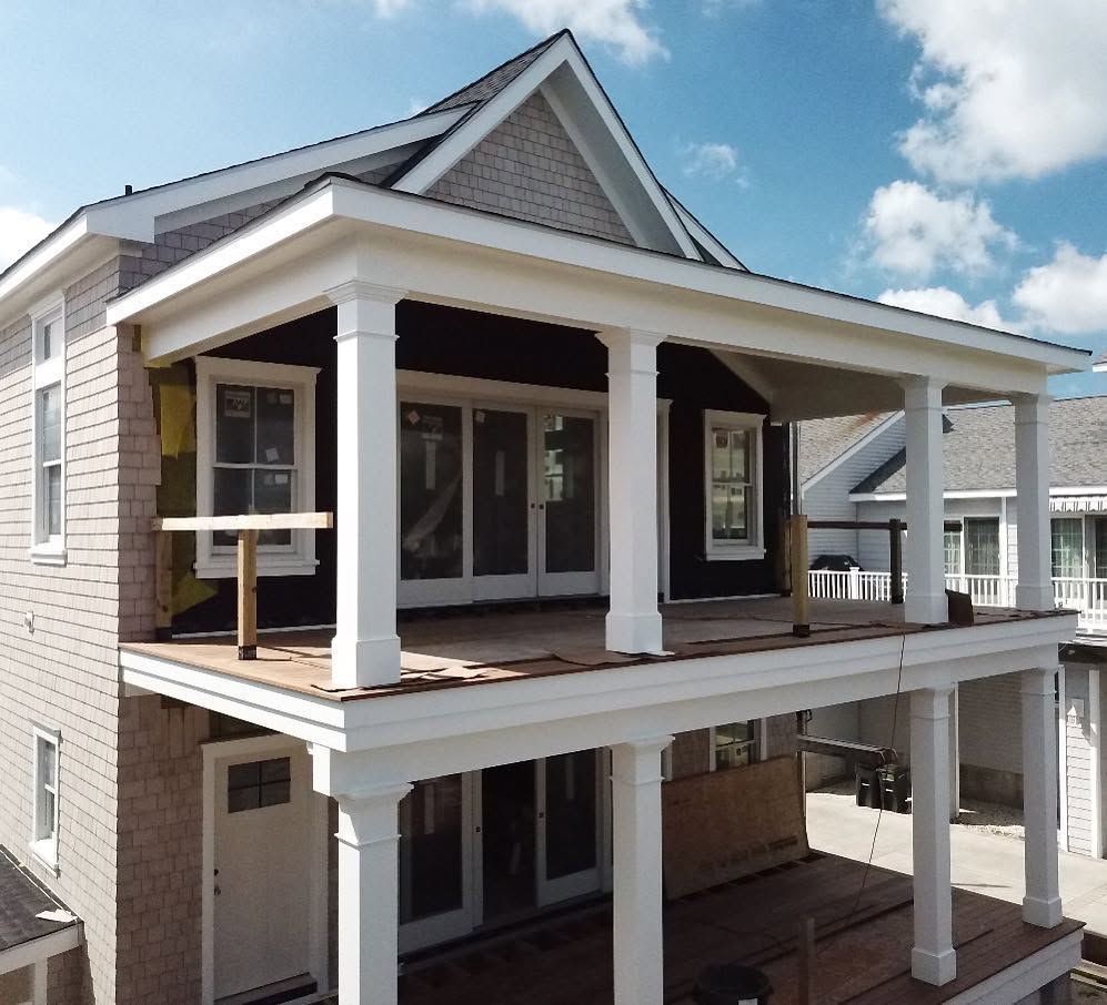 Two-story house with a front porch, white columns, and gray siding under construction