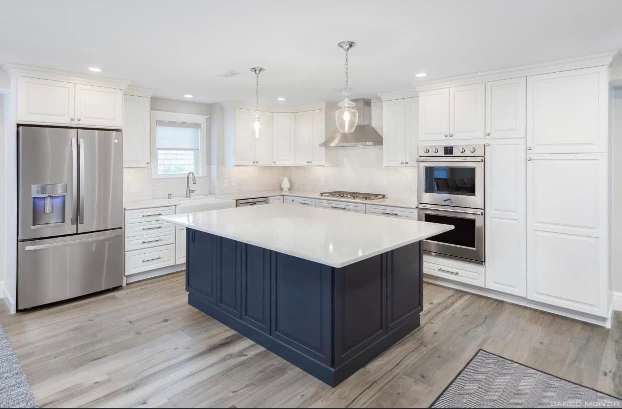 Bright modern kitchen with white cabinets, stainless steel appliances, and a navy island with white countertop