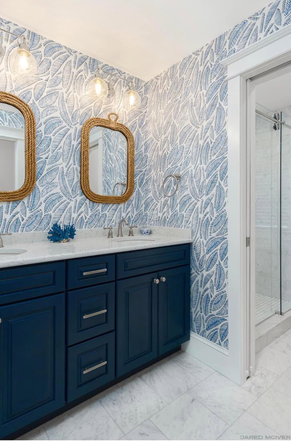 Elegant bathroom with navy vanity, gold-framed mirrors, and blue patterned wallpaper
