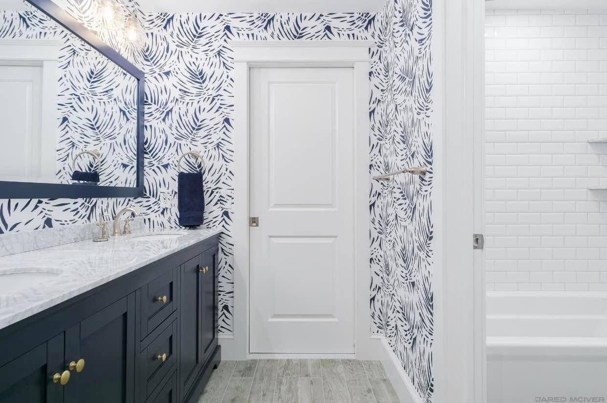 Modern bathroom with navy vanity, floral wallpaper, white door, and marble-look tile floor