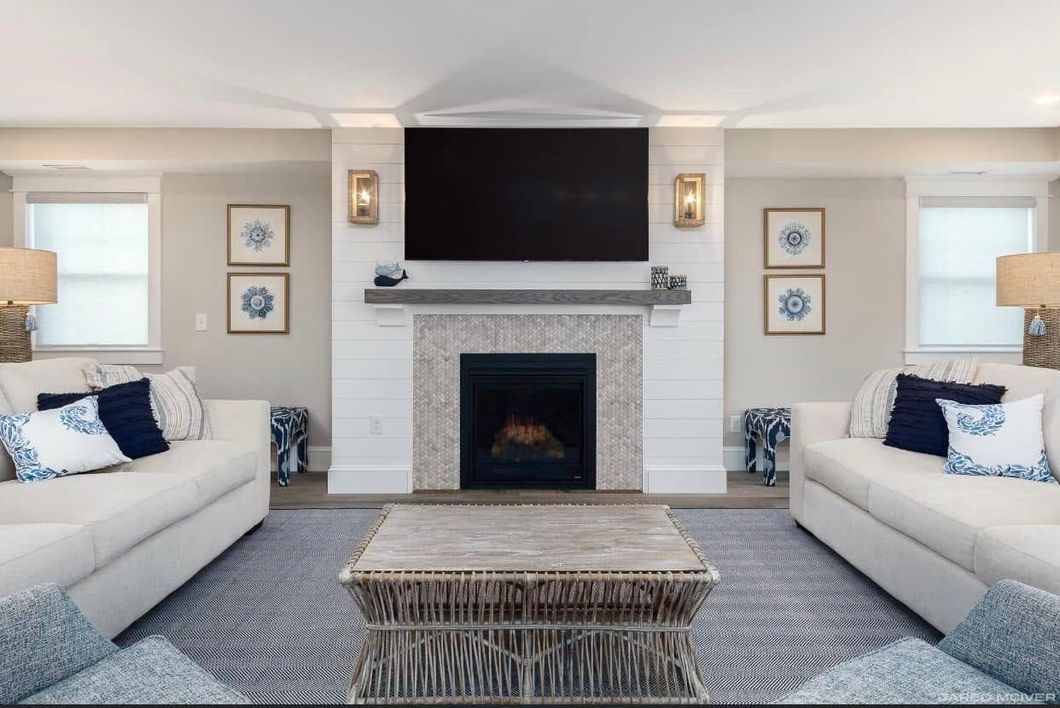 Bright symmetrical living room with two white sofas, central fireplace, and wall-mounted TV.
