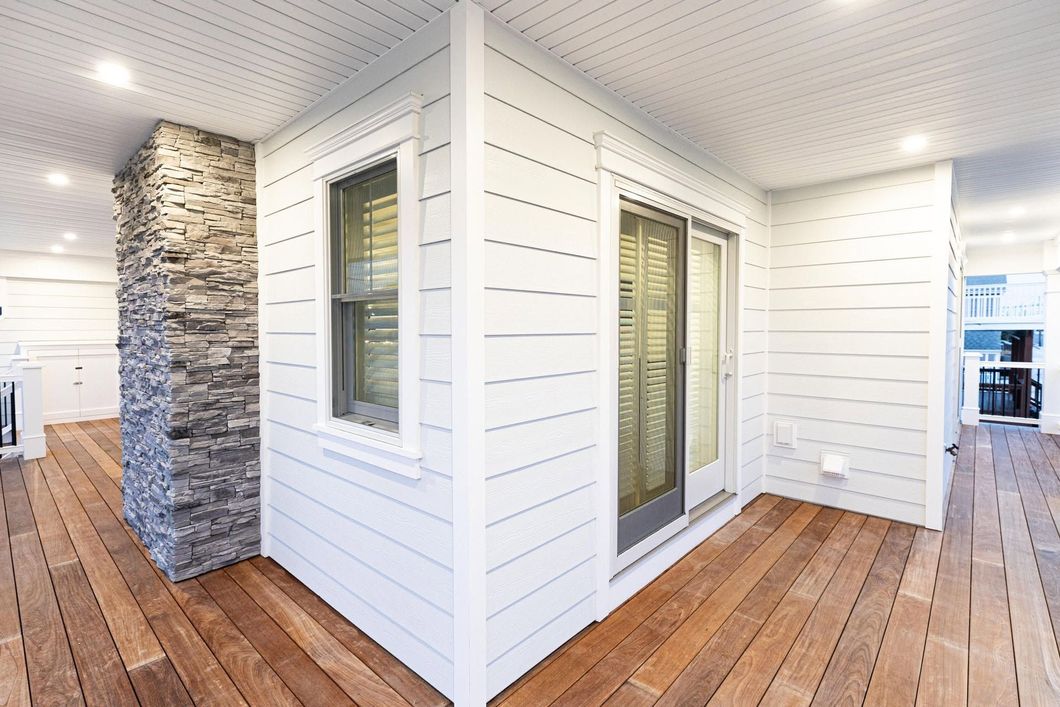 Modern home exterior with white siding, wood deck flooring, and stone accent columns