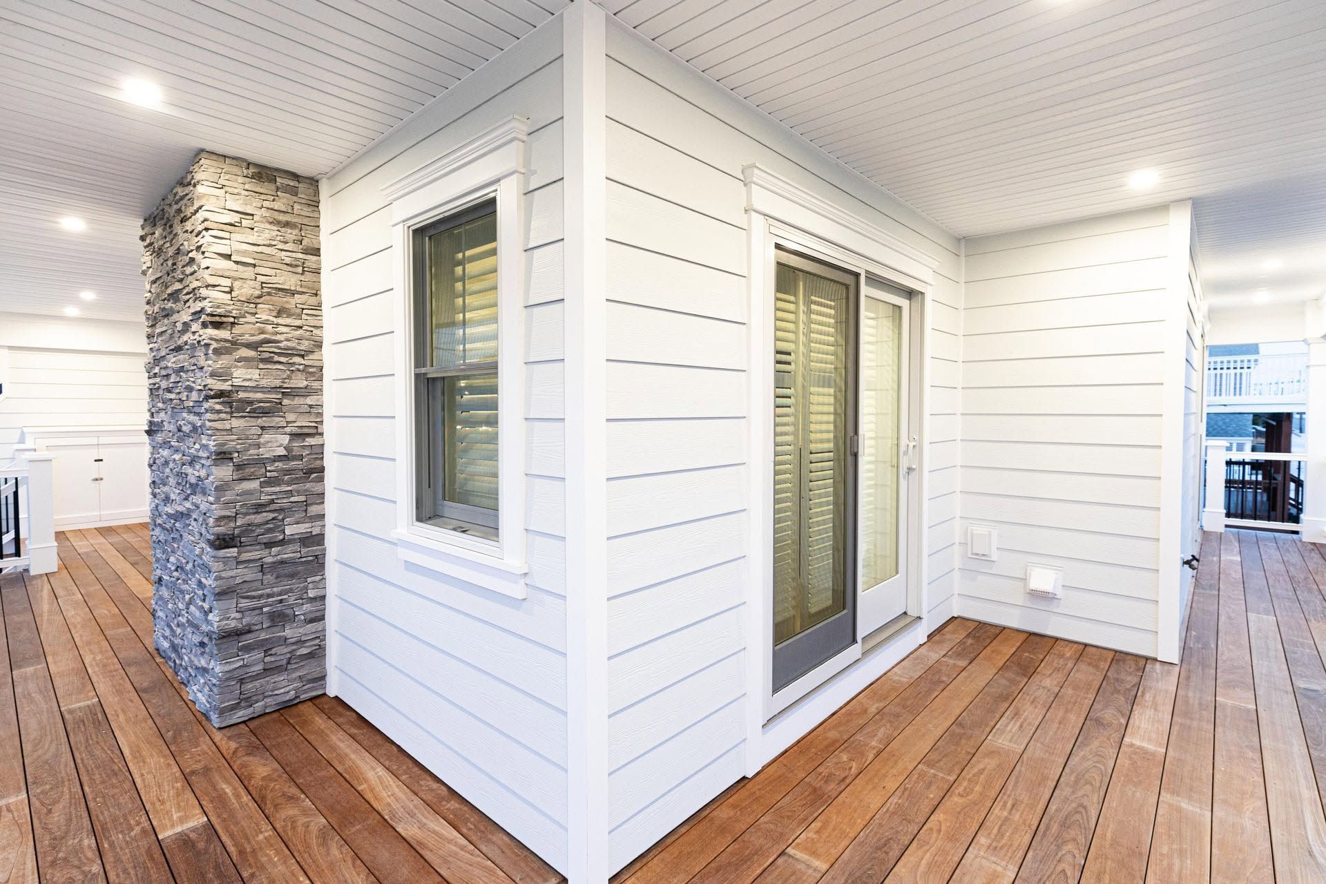 Modern white exterior porch with wood floors, stone column, and sliding glass doors