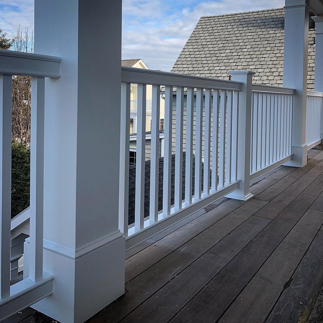White porch railing and weathered wooden deck with rooftops and blue sky beyond.