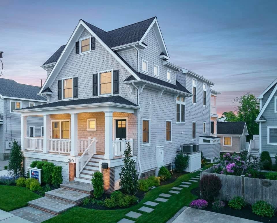 Large gray two-story house with white trim, lit porch, and manicured front yard at dusk