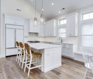 Bright white modern kitchen with island seating, stainless appliances, and wood floors