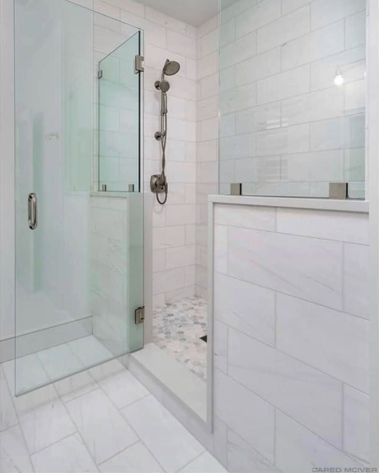 Modern white-tiled bathroom with glass shower, chrome fixtures, and half wall.