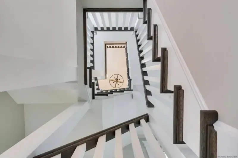 Bright white spiral staircase with dark wood railing leading down to a doorway with a decorative compass sign.