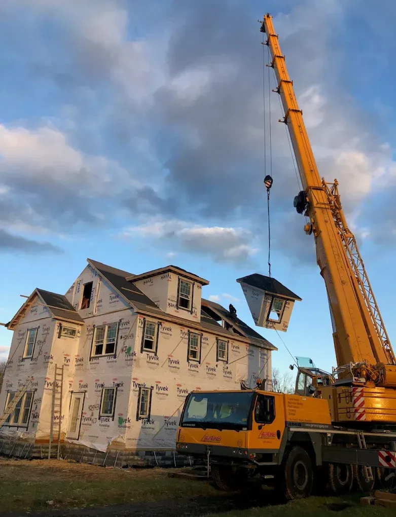 Yellow crane lifting a house roof at a construction site under a cloudy sky