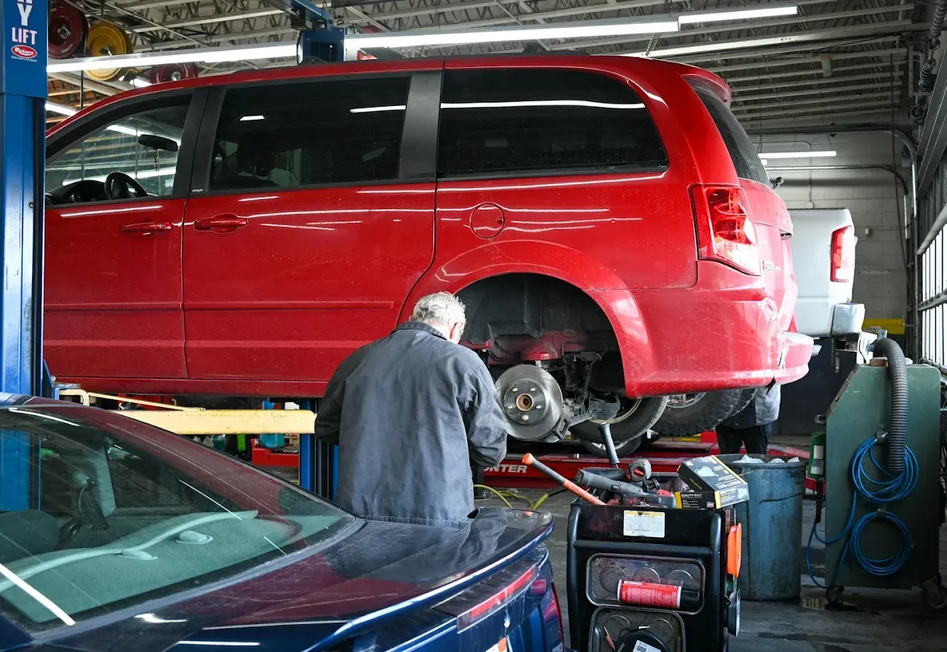 Mechanic working on a red minivan in an auto repair garage, with a car in the foreground. | Jones Complete Car Care