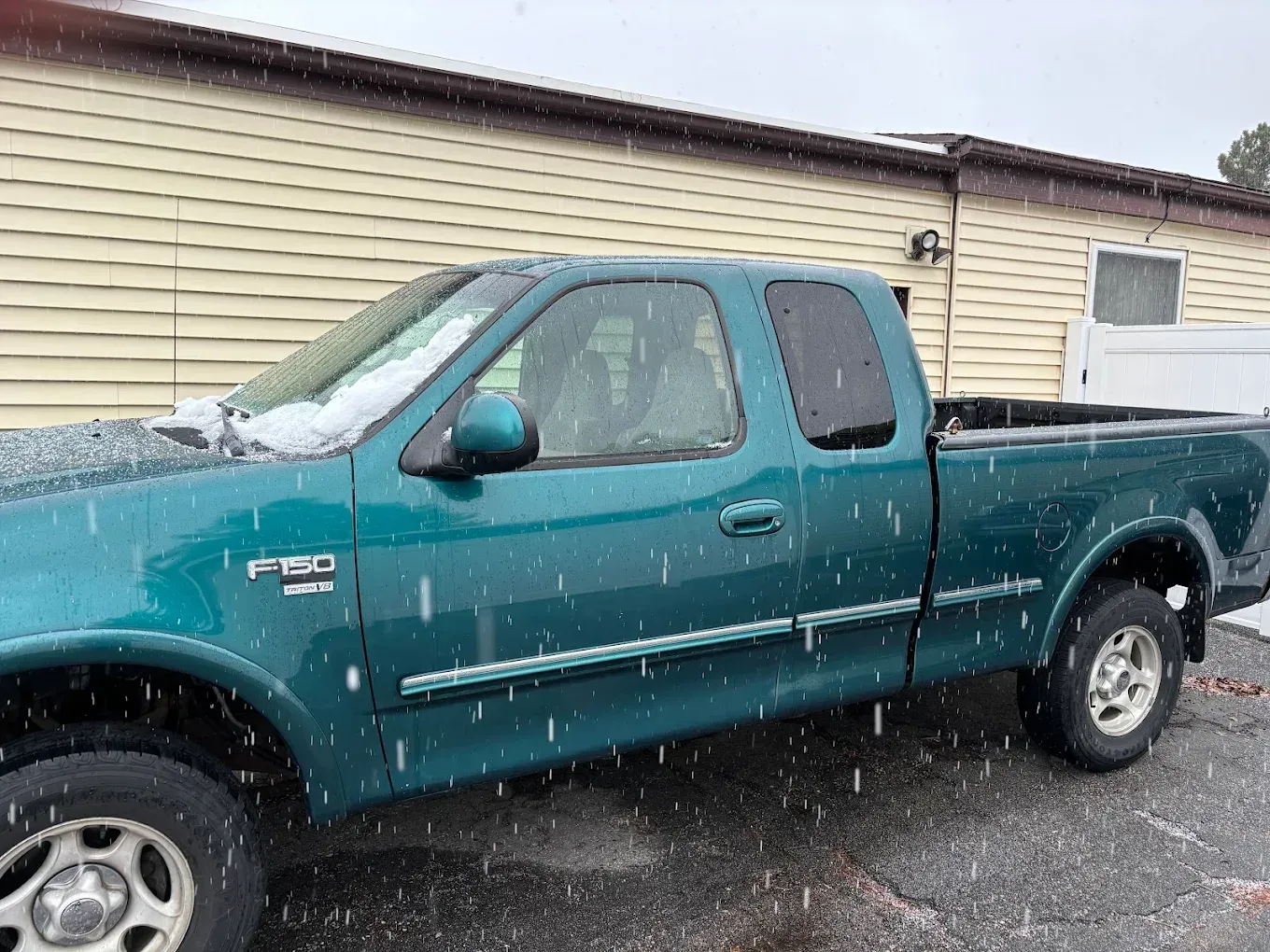 Teal Ford pickup truck parked in front of a beige building on a snowy day | Jones Complete Car Care