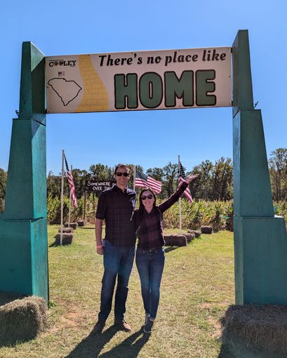 A man and woman standing under a sign that says there 's no place like home A man and woman standing under a sign that says there 's no place like home