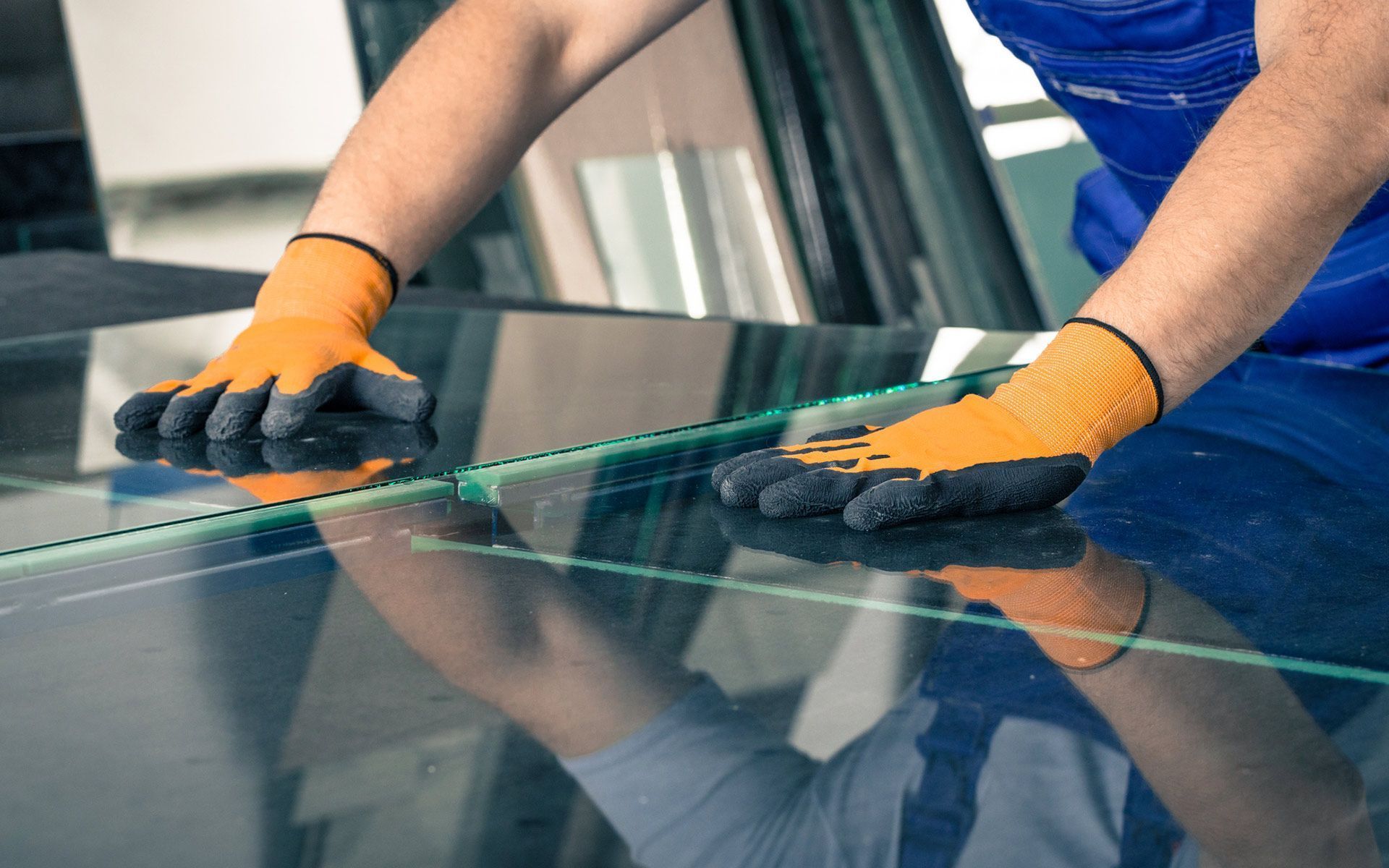 Person wearing orange work gloves working with glass.