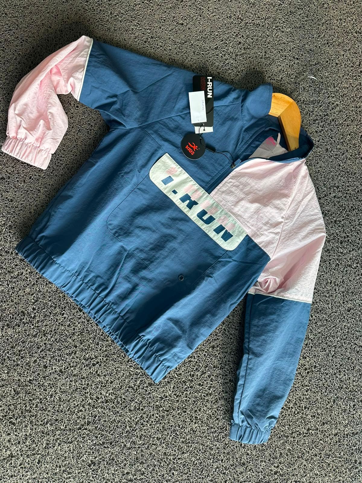 Camisa azul y rosa de manga larga con panel a rayas en el pecho, extendida sobre una alfombra gris.