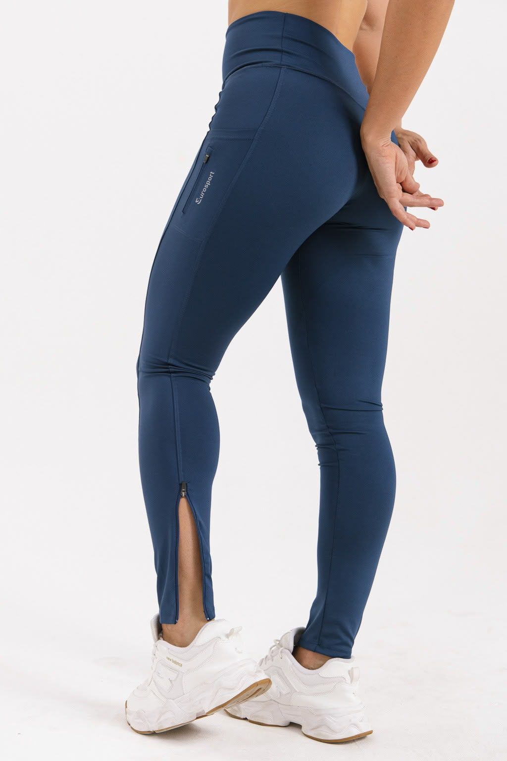 Vista trasera de una persona con leggings azul marino y zapatillas blancas, posando en un estudio.