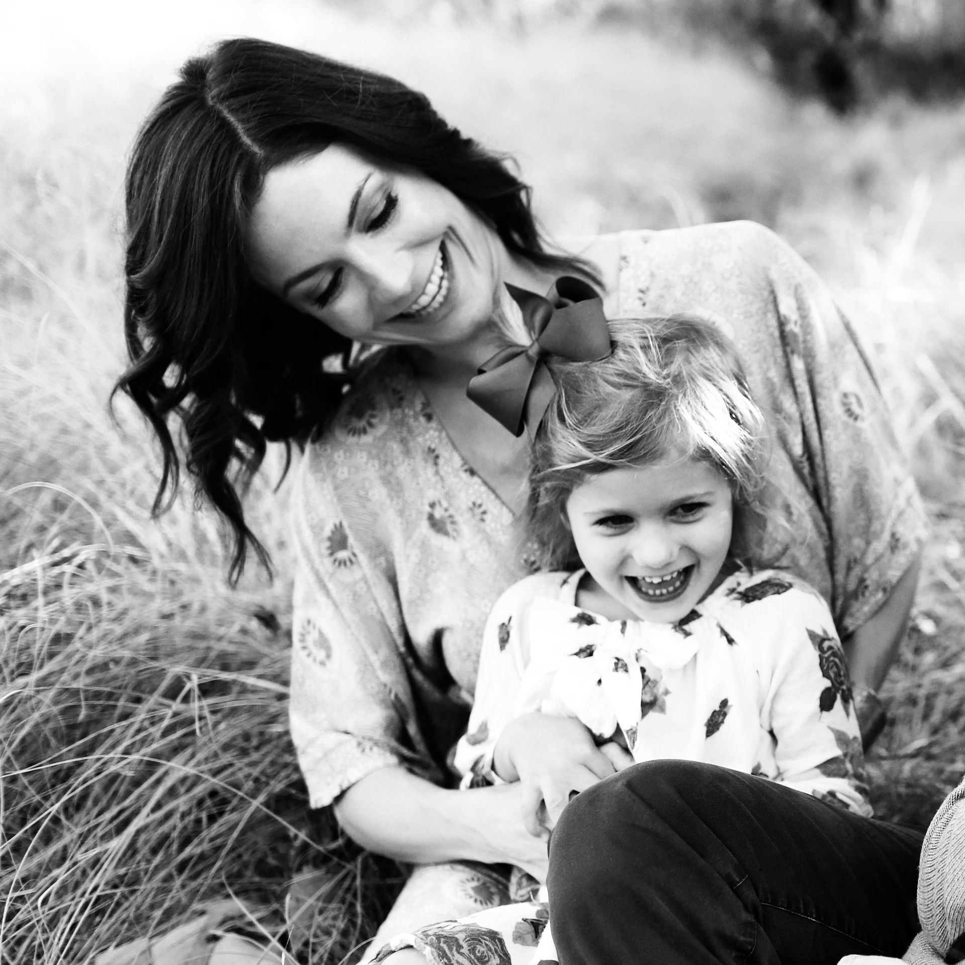 Woman smiles at laughing child outdoors, in grassy field.