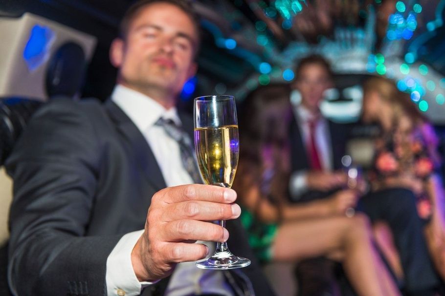Man in a suit toasting with a champagne flute at a party, with guests seated behind him