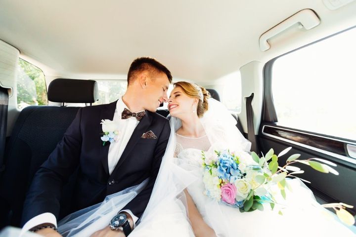 Newlyweds kissing in the back seat of a car, bride holding a colorful bouquet