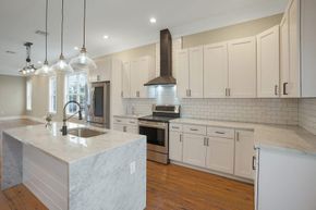 Modern kitchen with white cabinets, marble countertops, and stainless steel appliances. Island with sink and pendant lights overhead.