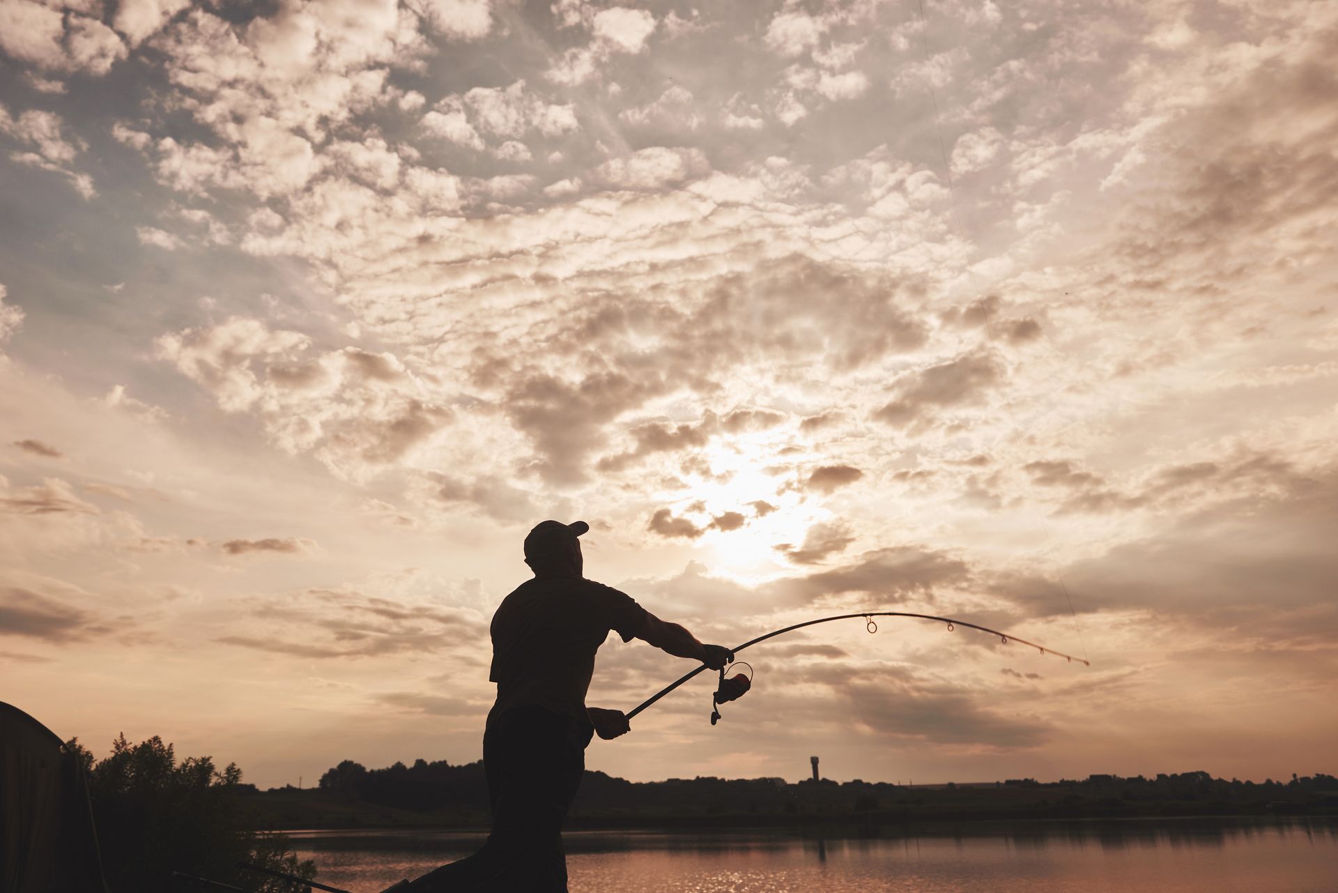 A man is fishing in a lake at sunset.
