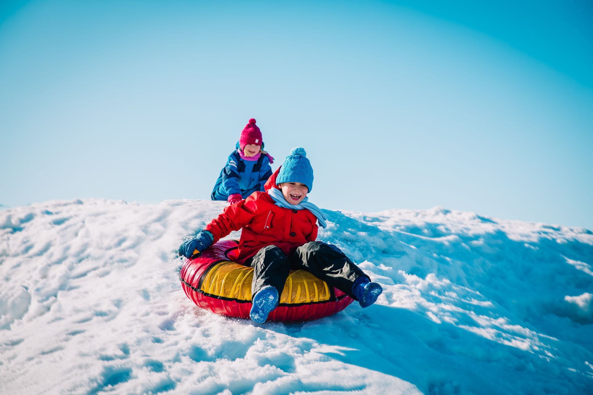 Two children are riding a snow tube down a snow covered hill.