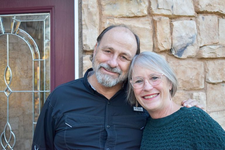 A man and a woman are posing for a picture in front of a stone wall.