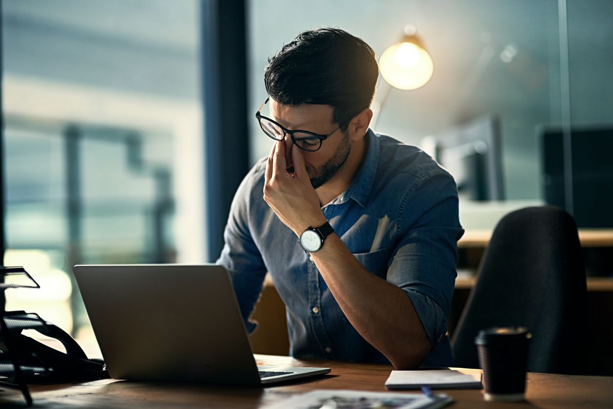 A young man sitting at his desk and considering his addiction to workaholism.