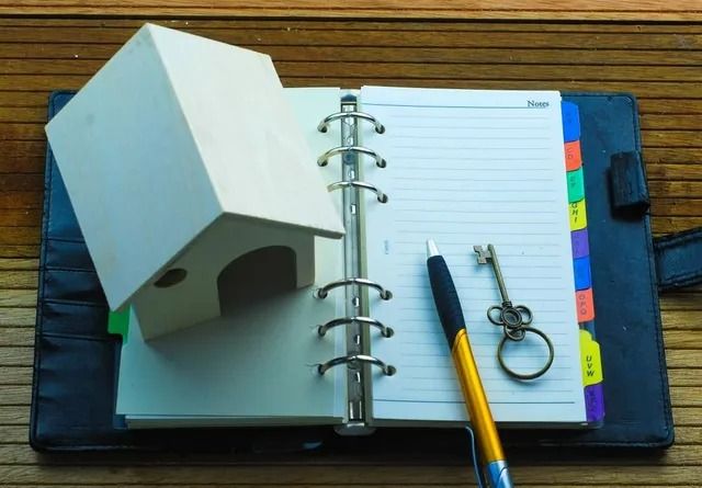 Small House Model on Notebook with Pen and Key — All Finanz & Insurance Solutions Mackay in Airlie Beach, QLD