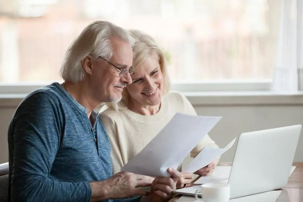 Older Couple Looking at Paperwork with Laptop and Coffee on Table — All Finanz & Insurance Solutions Mackay in Cannovale, QLD