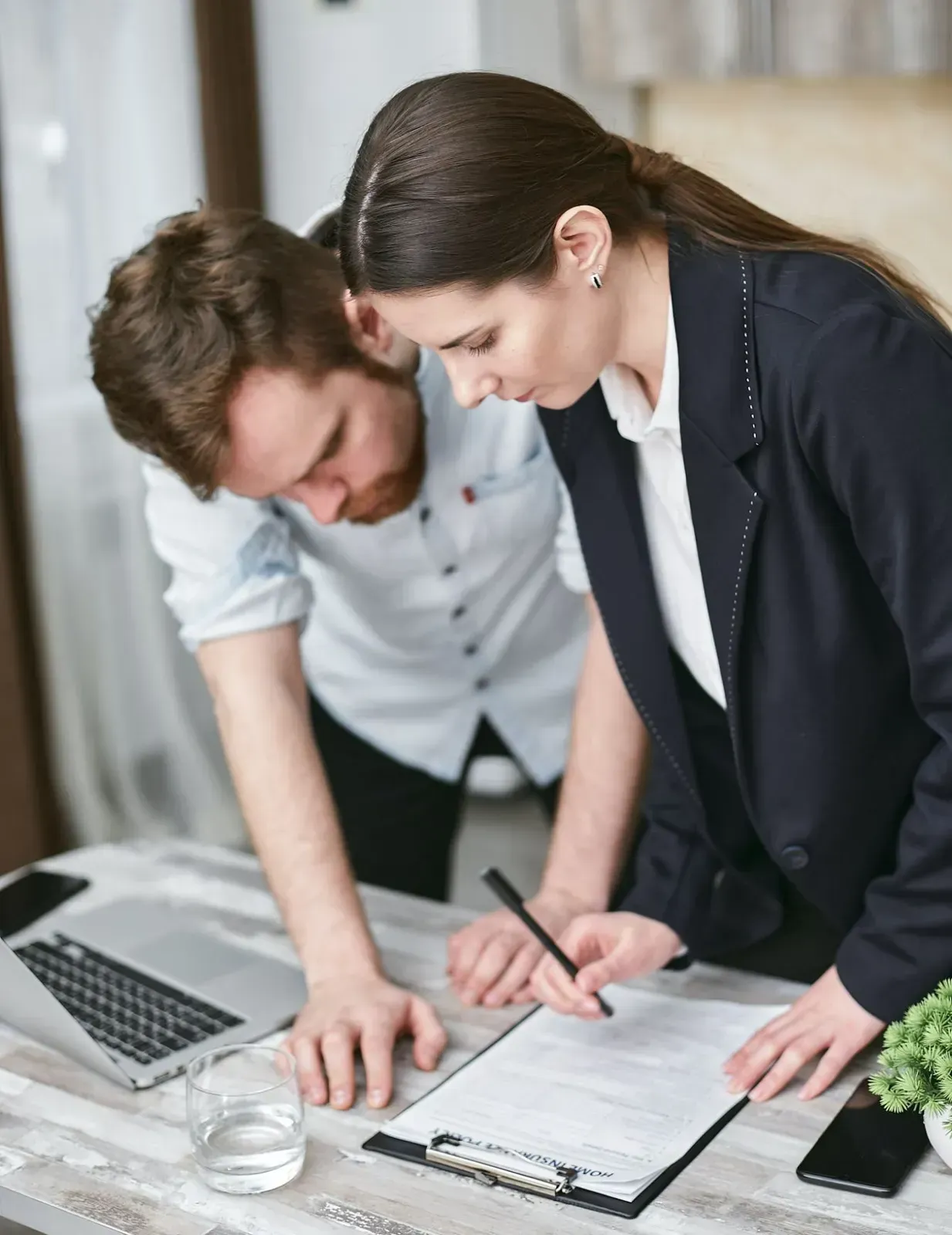 Woman in Suit Pointing to Document with Man Leaning Over Table — All Finanz & Insurance Solutions Mackay in North Mackay, QLD