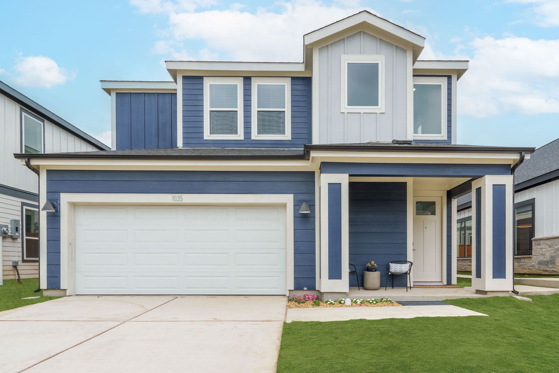 Two-story house with blue siding, white trim, and a two-car garage. Green lawn and blue sky.