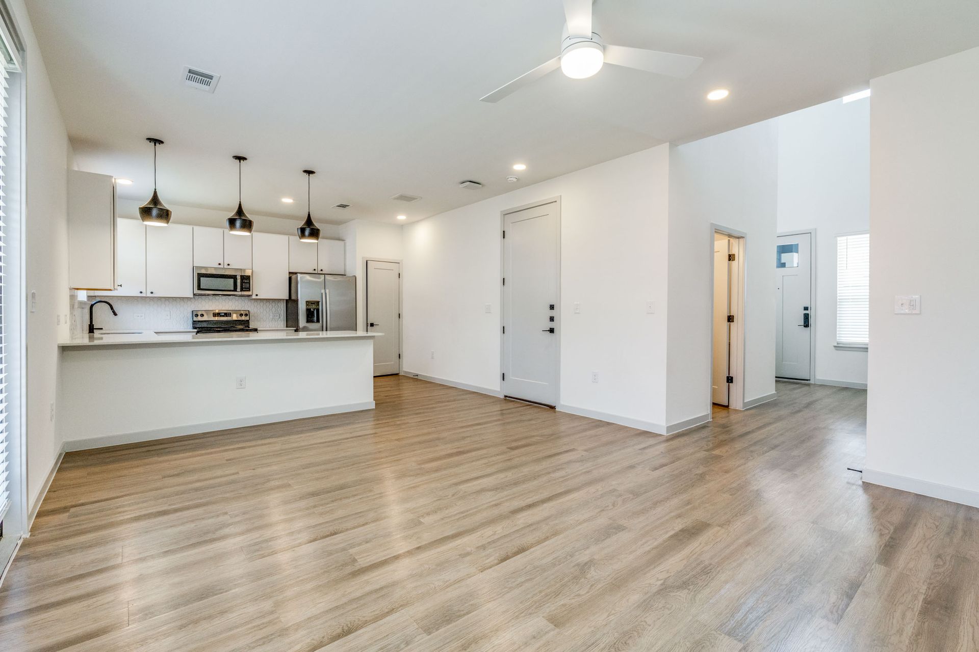 Modern open-concept living space with kitchen, white cabinets, wood floors, and a ceiling fan.