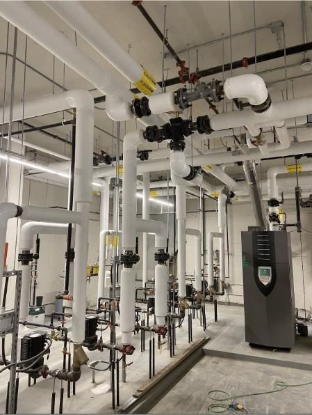 Pipes and valves in a mechanical room. White insulated pipes, gray equipment, and concrete floor.