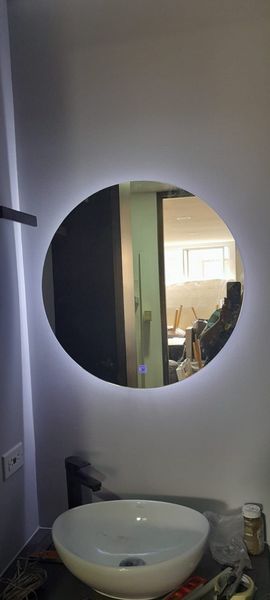 Lavabo con espejo redondo retroiluminado que refleja una habitación al fondo