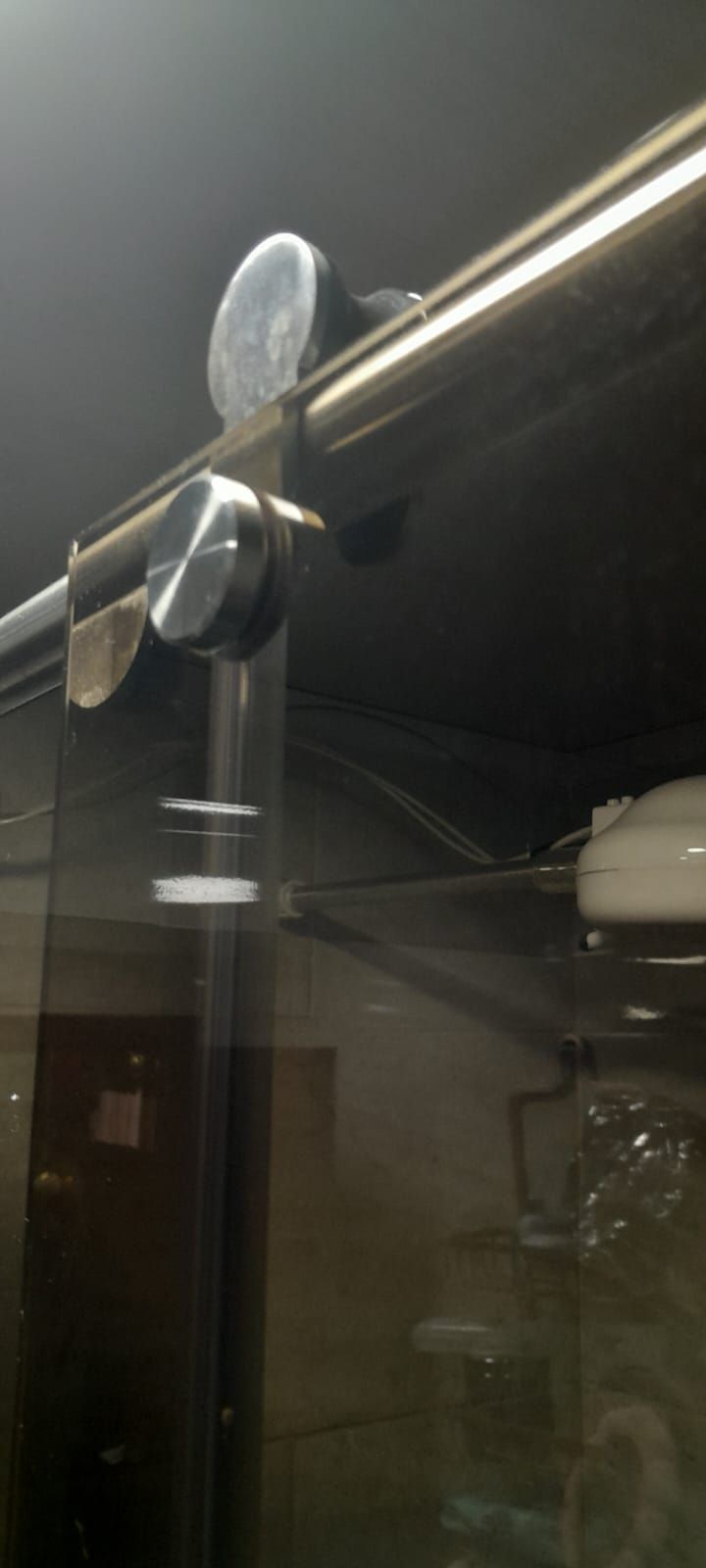 Primer plano de una abrazadera metálica sujeta a una barra horizontal sobre un fondo de vidrio oscuro