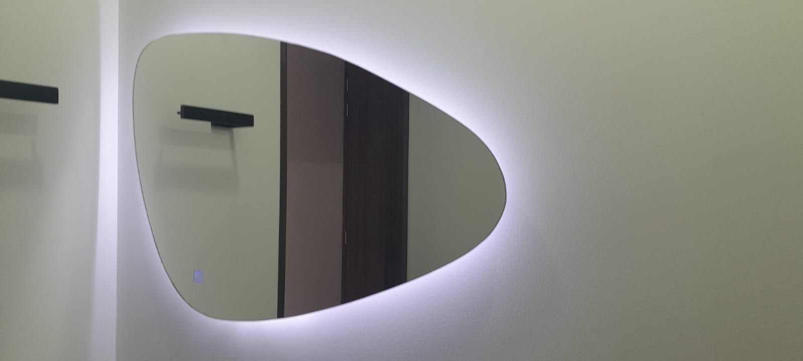Espejo de pared en forma de lágrima que refleja un pasillo con un aplique en una pared blanca