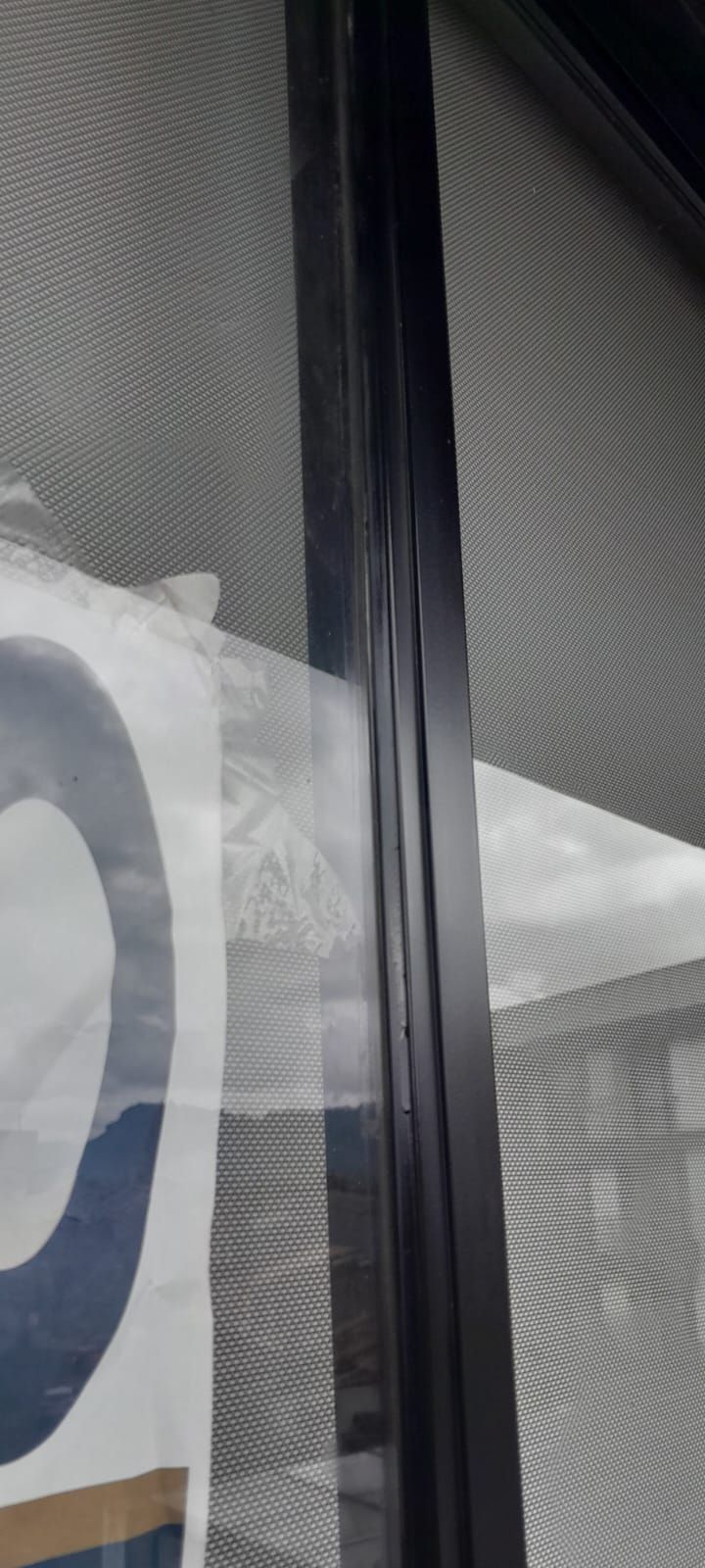Primer plano de una ventana con marco vertical negro y reflejos en el vidrio texturizado