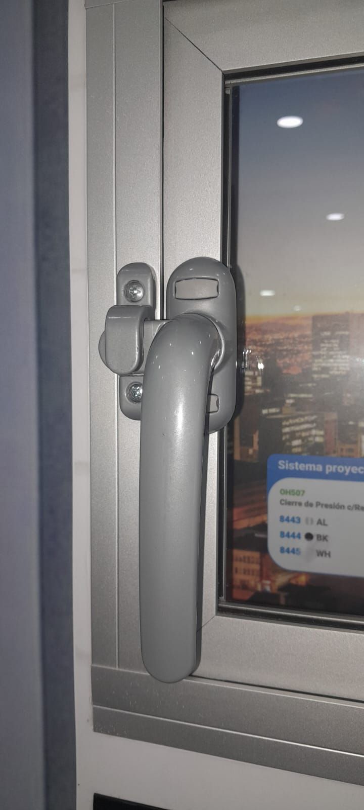 Primer plano de una manija gris con cerradura en una ventana corrediza al anochecer.