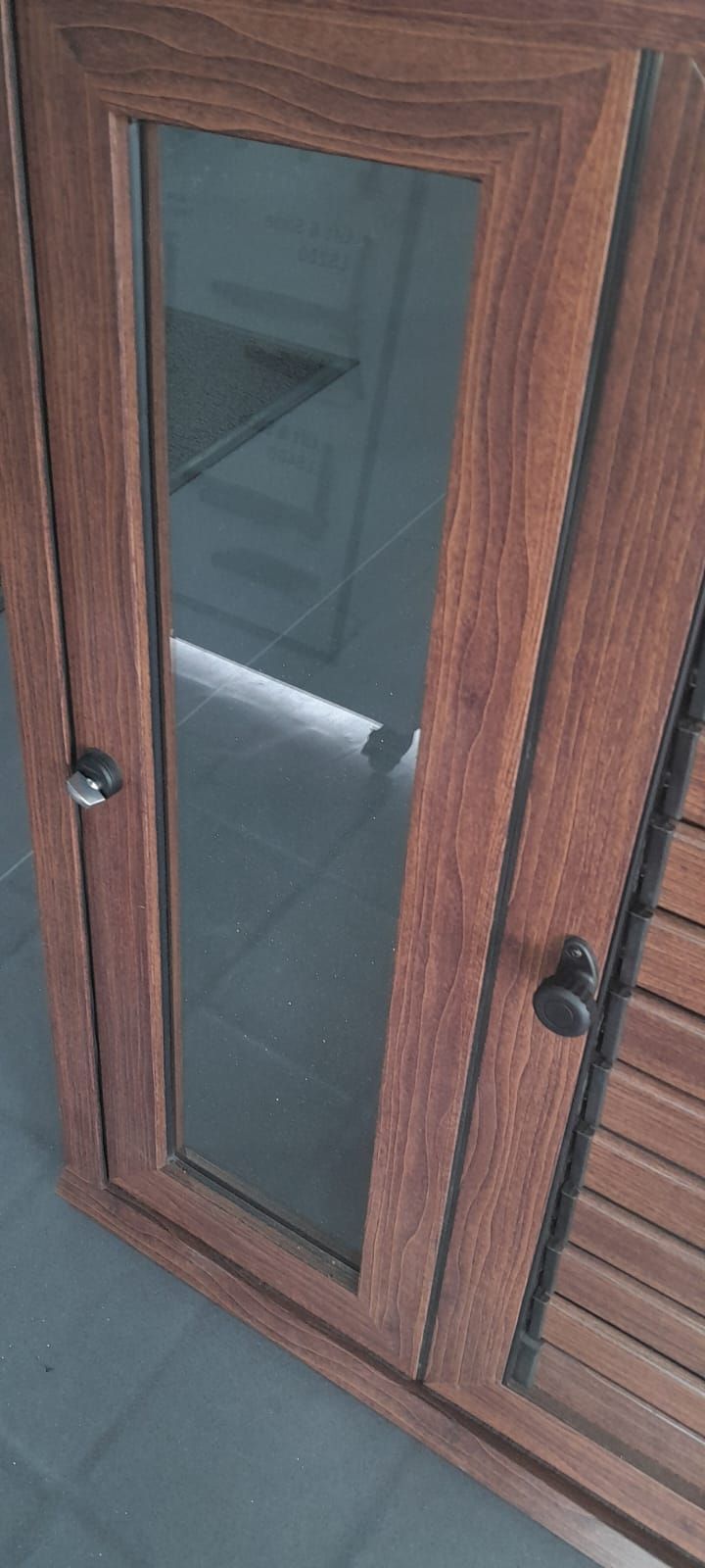 Puerta o armario de madera con paneles de vidrio y dos pomos redondos negros, visto en ángulo