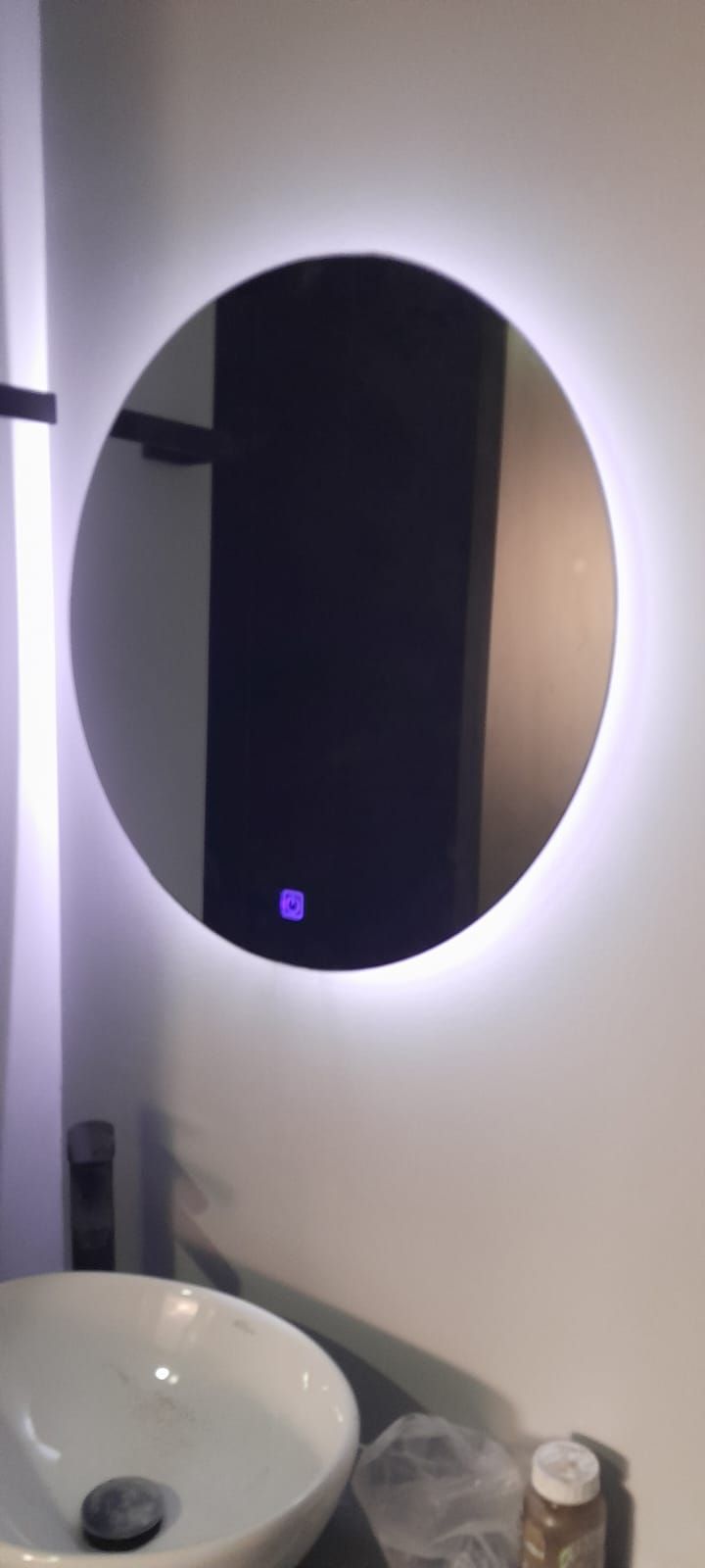 Espejo redondo retroiluminado sobre un lavabo blanco en un baño