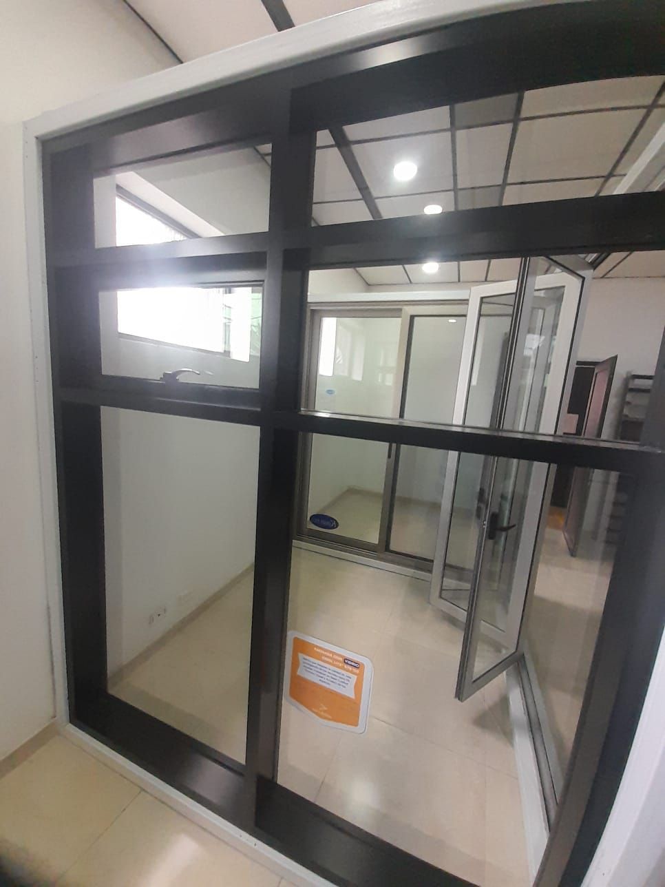 Entrada de oficina de cristal con marcos metálicos negros y una puerta abierta en un pasillo luminoso