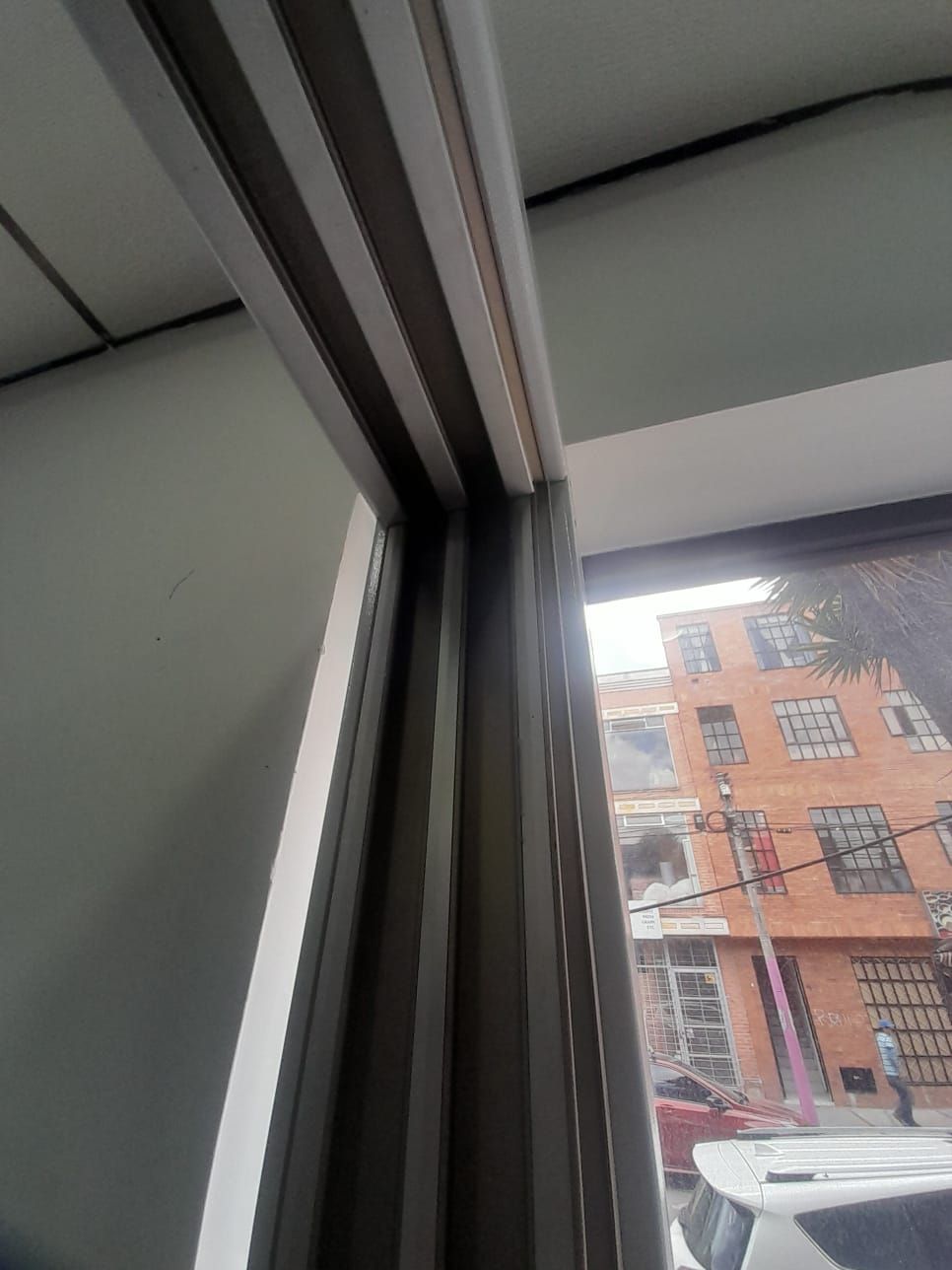 Ventana entreabierta con vistas a un edificio de ladrillo y a un coche aparcado en el exterior